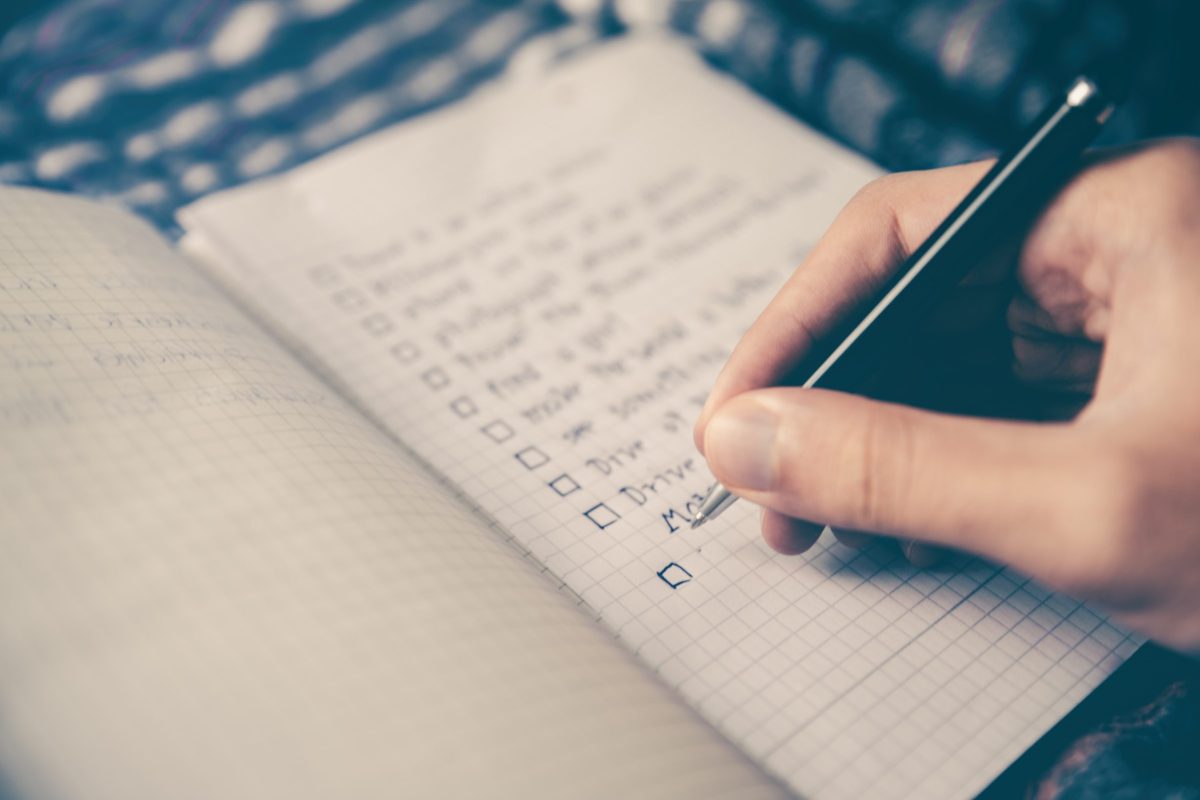 A hand writing a checklist in a grid-ruled notebook