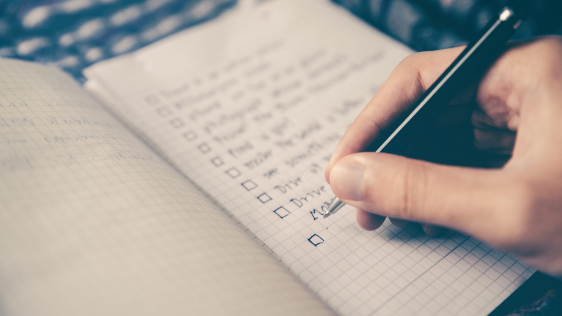 A hand writing a checklist in a grid-ruled notebook